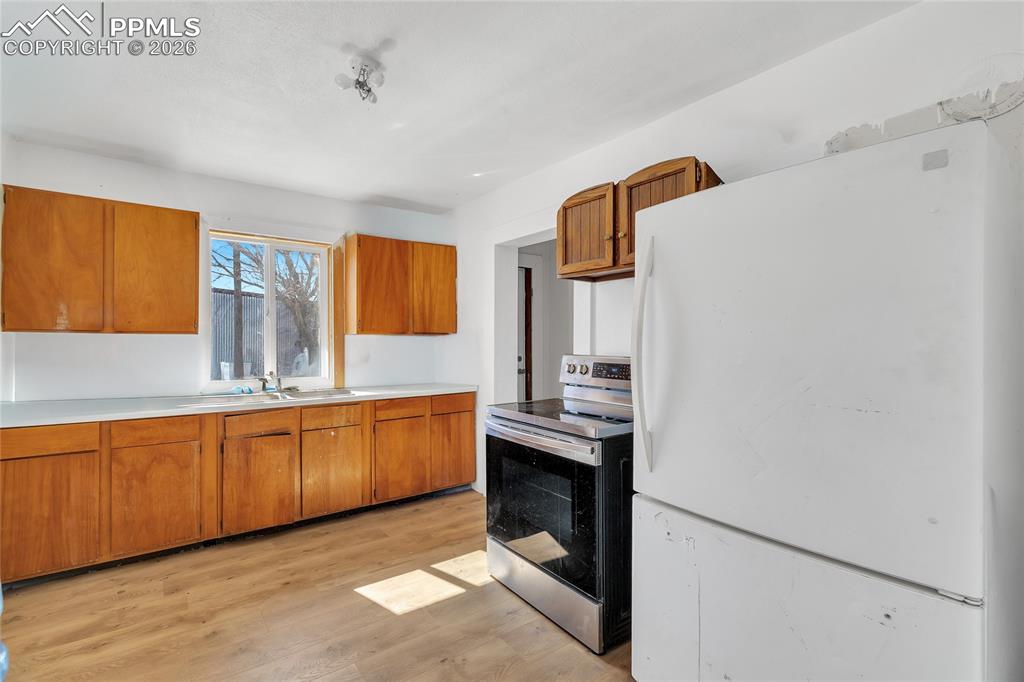 ADU Kitchen featuring freestanding refrigerator, stainless steel electric range oven, wood finish cabinetry, light countertops, and light wood-type flooring