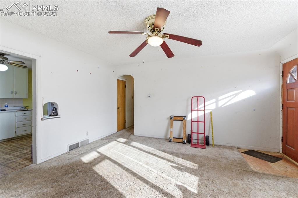 Unfurnished living room featuring a ceiling fan, carpet floors, arched walkways, and a textured ceiling