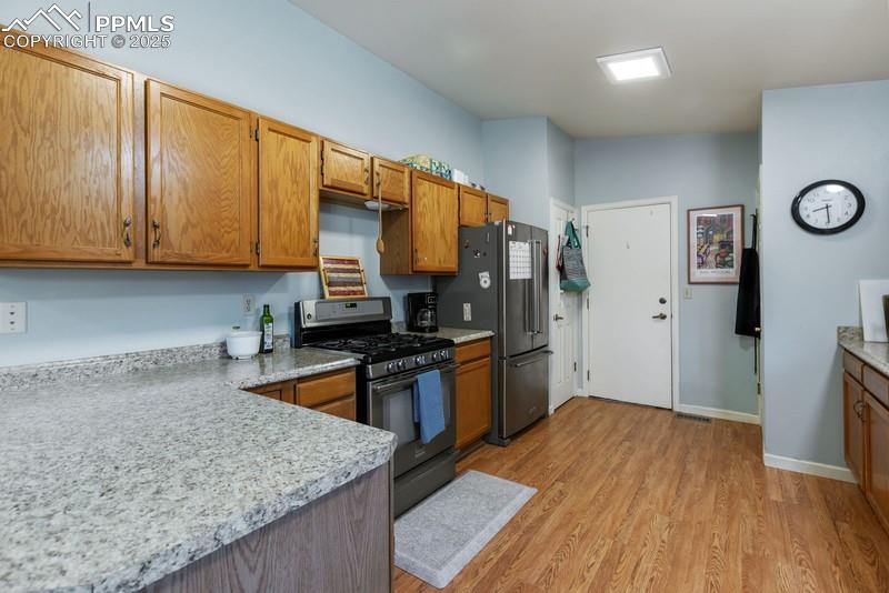 Kitchen featuring range with gas stovetop, light wood-style floors, brown cabinetry, light countertops, and high end refrigerator