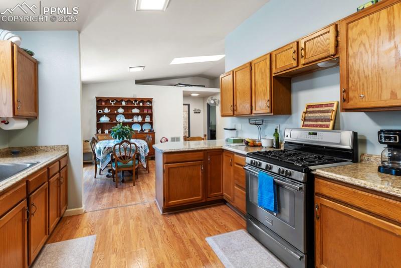 Kitchen featuring gas range, brown cabinetry, lofted ceiling, light wood-style flooring, and a peninsula