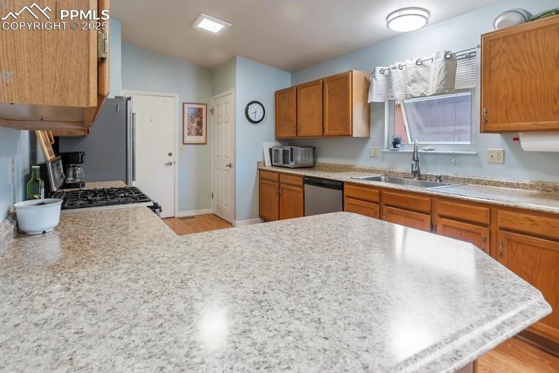 Kitchen with brown cabinets, light wood-style floors, stainless steel appliances, and a peninsula