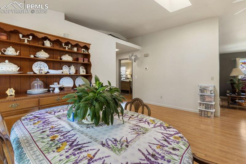 Dining space featuring light wood-style flooring, a skylight, and vaulted ceiling