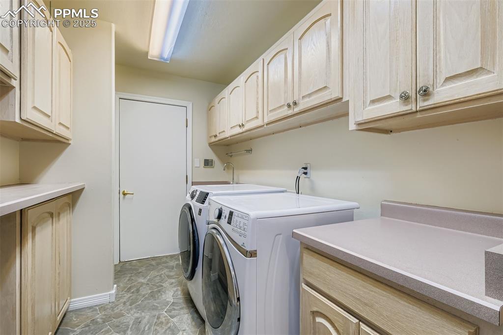 Laundry room featuring washer and clothes dryer, cabinet space, and light stone finish floors (main floor with door to garage)