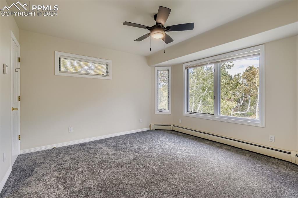 Carpeted bedroom featuring a baseboard radiator, multiple windows, and a ceiling fan, ensuite bathroom (upper floor)