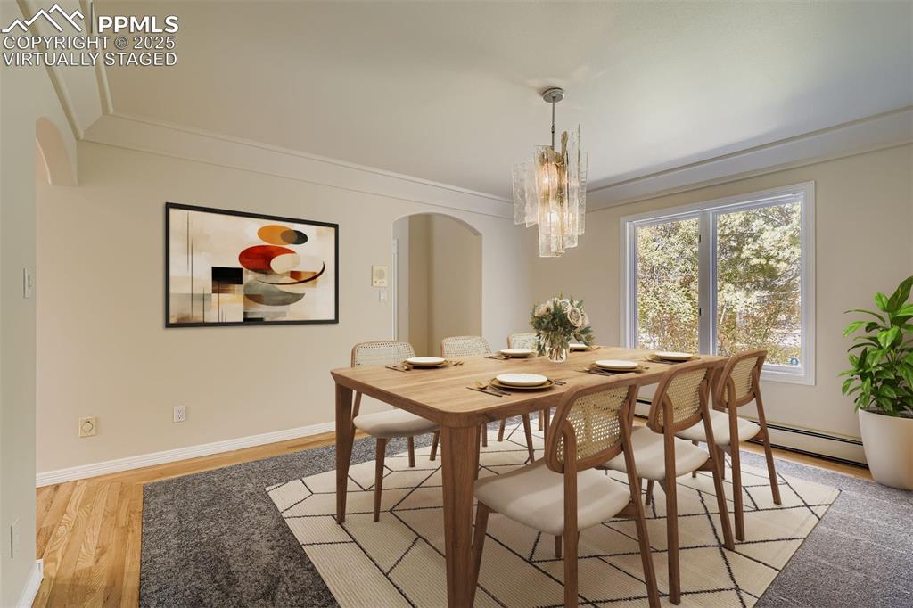 Virtually Staged! Formal dining room with arched walkways, light wood-style flooring, a chandelier (included), crown molding, and a baseboard heating unit (main floor)