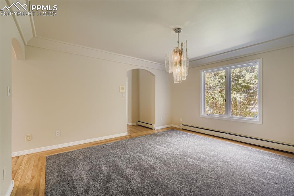 Formal dining room featuring arched walkways, light wood-style floors, a baseboard radiator, a baseboard heating unit, and a chandelier (included)