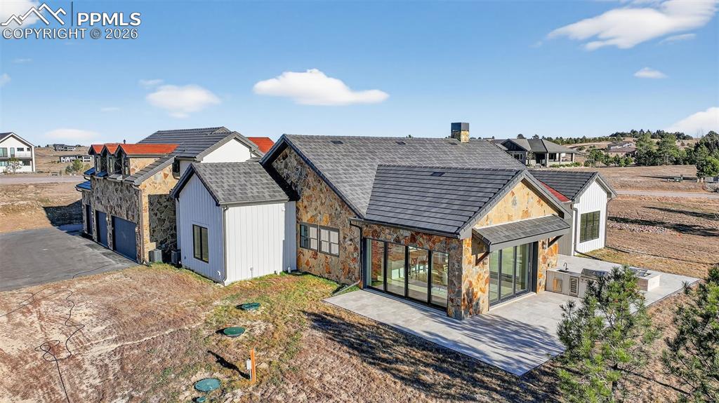 Back of property with stone siding, a patio, a garage, and a residential view