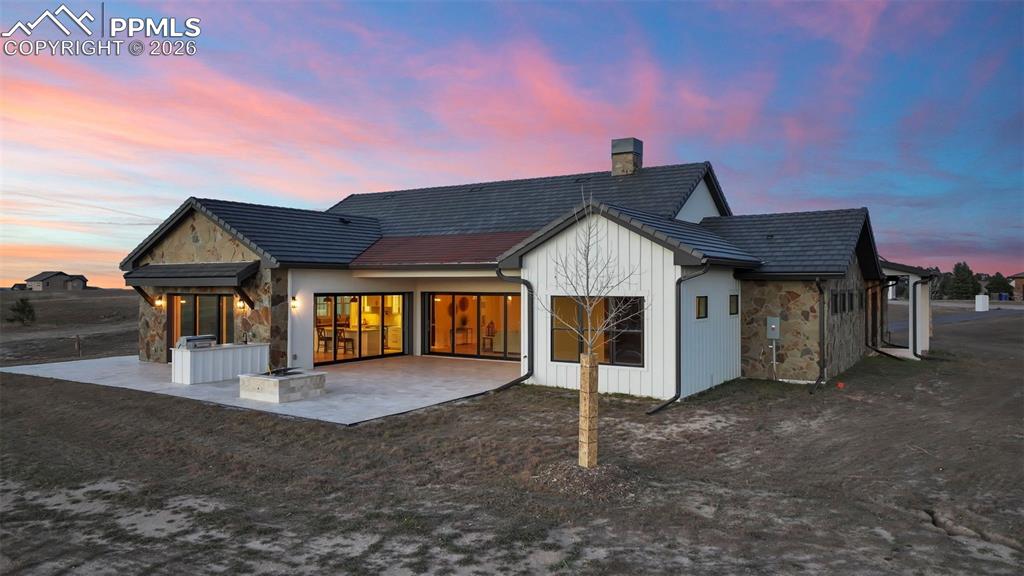 Rear view of property with a patio area, stone siding, a chimney, and board and batten siding