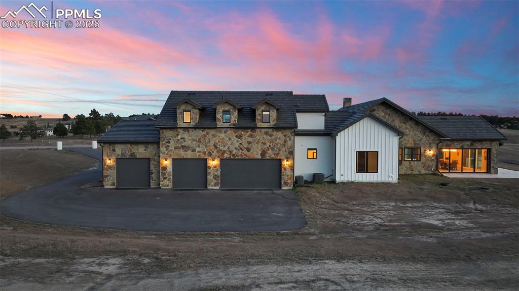 View of front of home featuring stone siding, board and batten siding, driveway, a garage, and a chimney