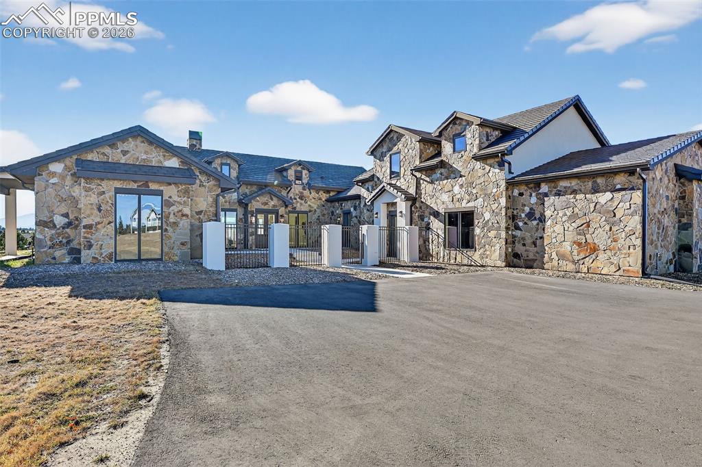 French country inspired facade featuring stone siding, a chimney, a fenced front yard, and a gate
