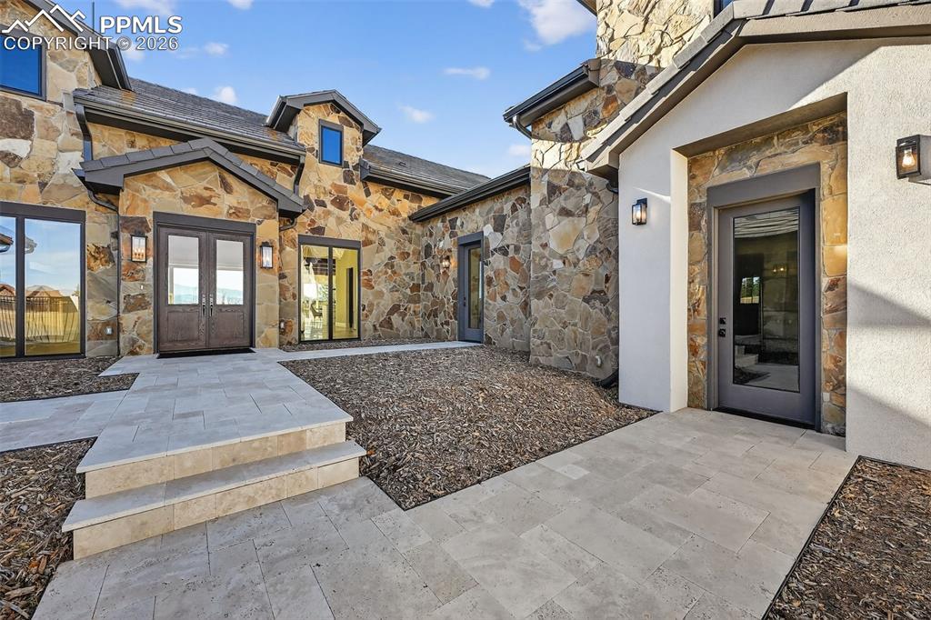 Doorway to property featuring stone siding, french doors, and stucco siding
