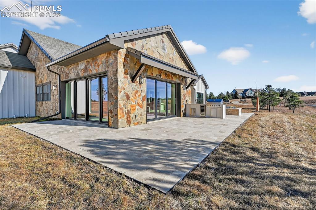 Rear view of house featuring stone siding and an outdoor kitchen