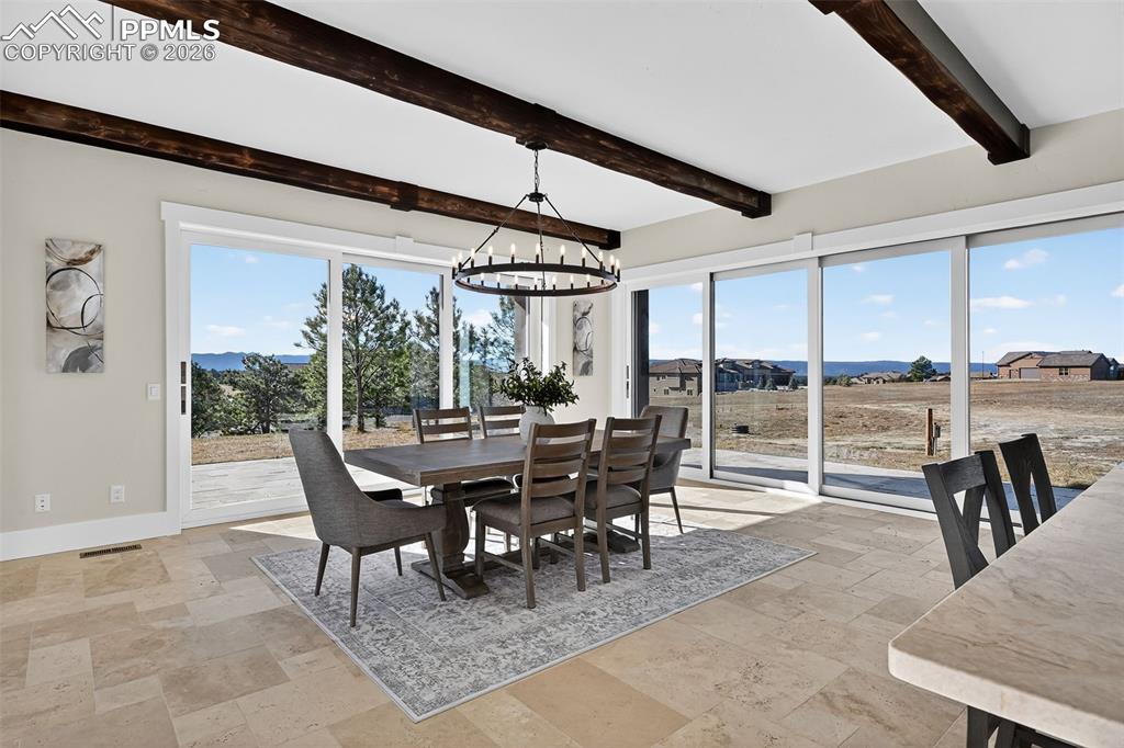 Dining room featuring a chandelier, stone tile flooring, beamed ceiling, and a mountain view