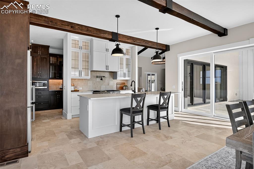 Kitchen with glass fronted cabinets, pendant lighting, a breakfast bar area, backsplash, and light stone finish flooring