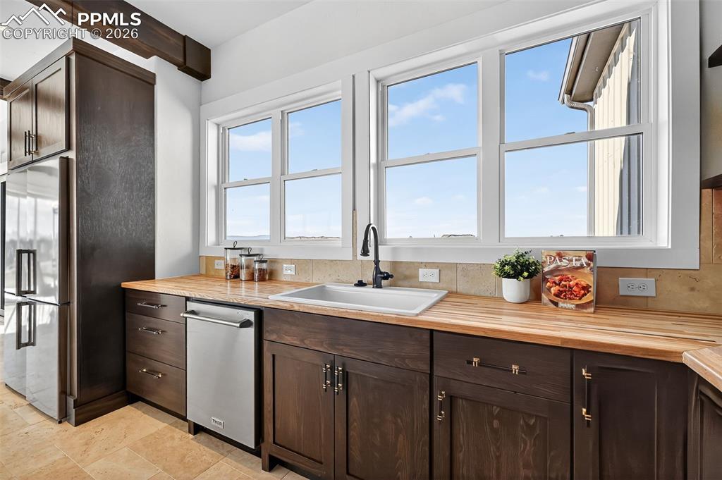 Kitchen featuring dark wood finish cabinetry, stainless steel appliances, butcher block countertops, and beam ceiling