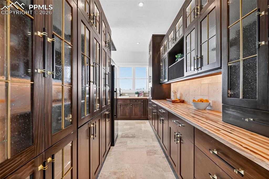 Bar featuring glass insert cabinets, dark wood finish cabinetry, decorative backsplash, stone tile floors, and recessed lighting
