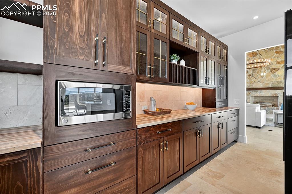 Kitchen featuring stainless steel microwave, glass fronted cabinets, wooden counters, dark wood finish cabinets, and open shelves