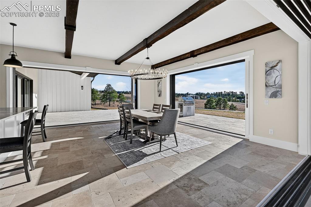Dining area featuring stone tile flooring, hanging lights, and beamed ceiling