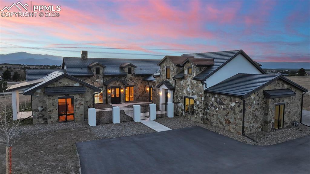 View of front of property featuring stone siding, a fenced front yard, a tile roof, and a chimney