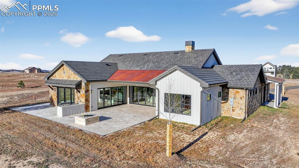 Rear view of house with stone siding, a patio area, and a chimney