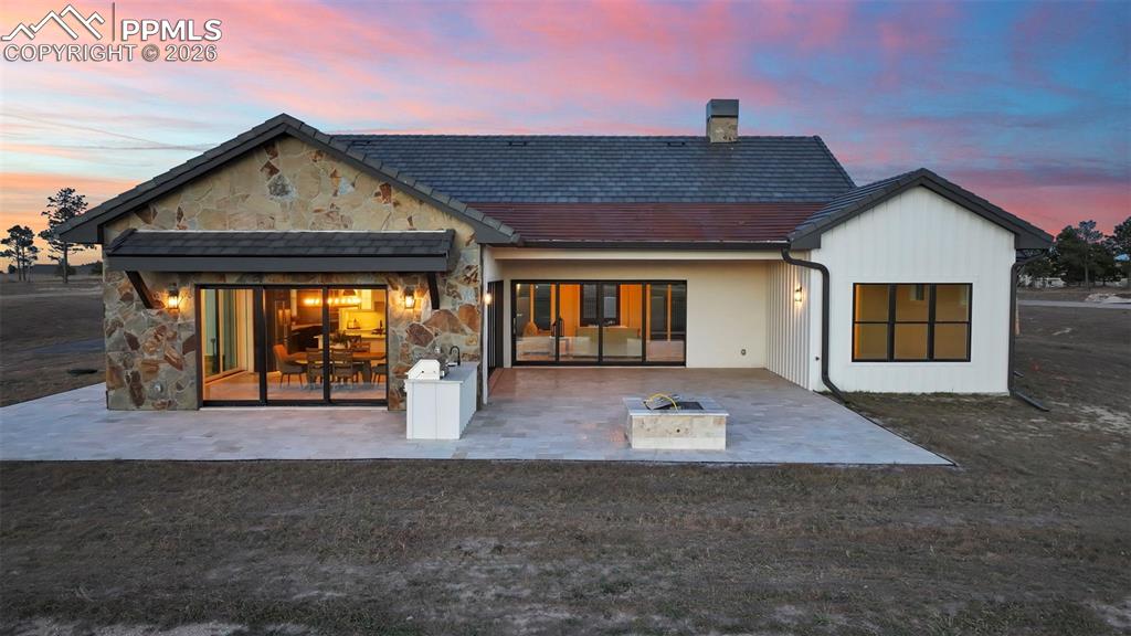 Back of property featuring stone siding, a chimney, and a patio area
