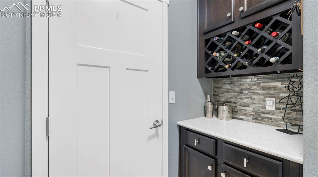Bar area with decorative backsplash, dark wood finish cabinets, and light stone counters