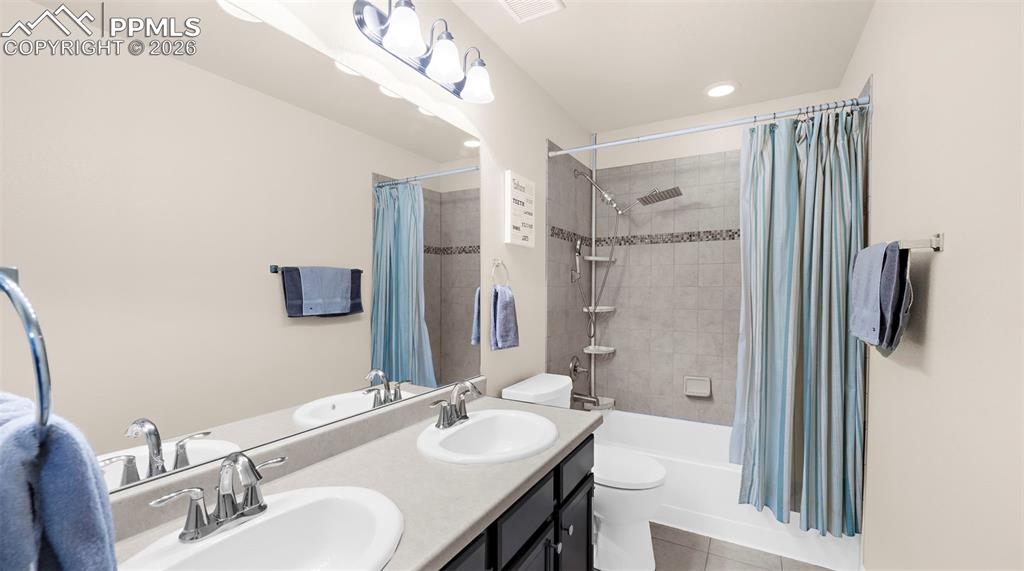 Bathroom with double vanity, shower / bathtub combination with curtain, and light tile patterned flooring