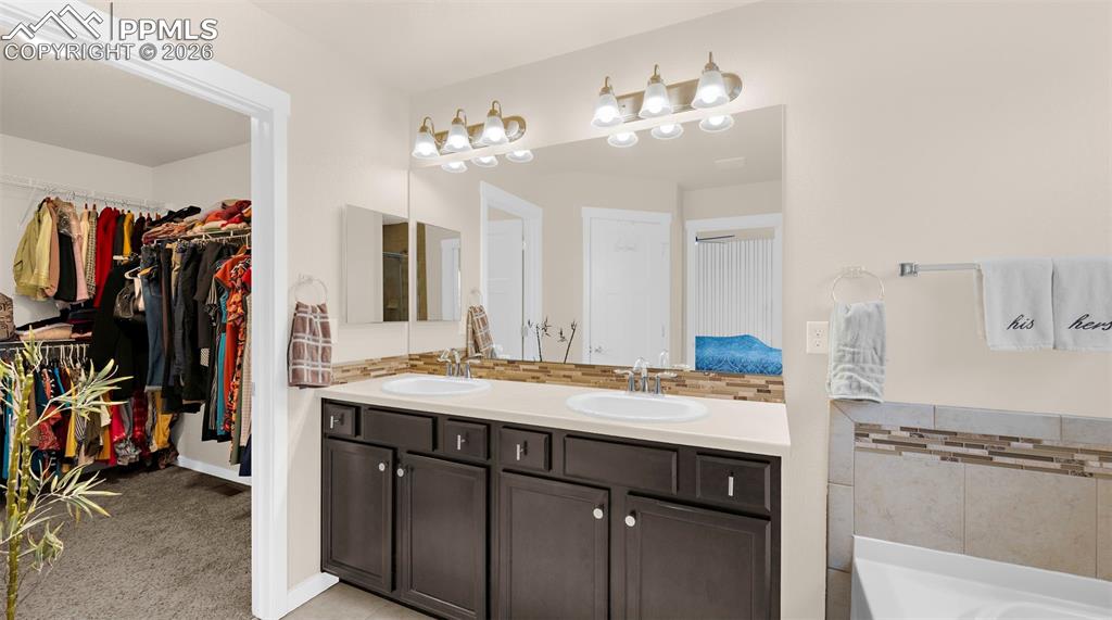 Ensuite bathroom with backsplash, double vanity, a walk in closet, light carpet, and a bath