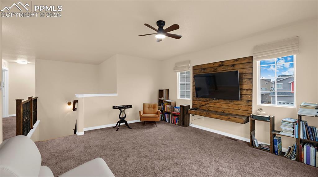 Living area with an upstairs landing, carpet, ceiling fan, and plenty of natural light