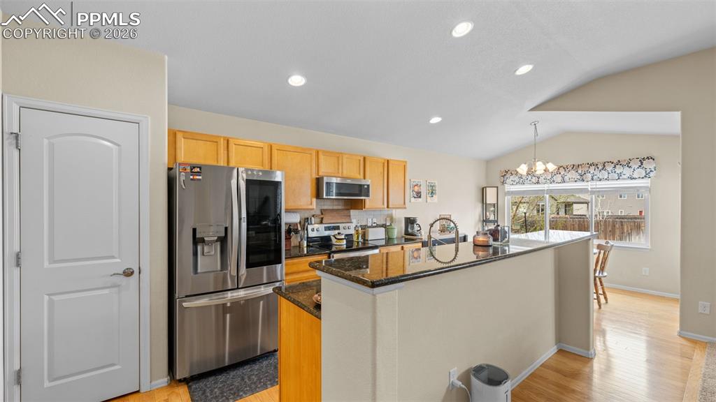 Kitchen featuring an island with sink, stainless steel appliances, dark stone counters, a chandelier, and light wood finished floors