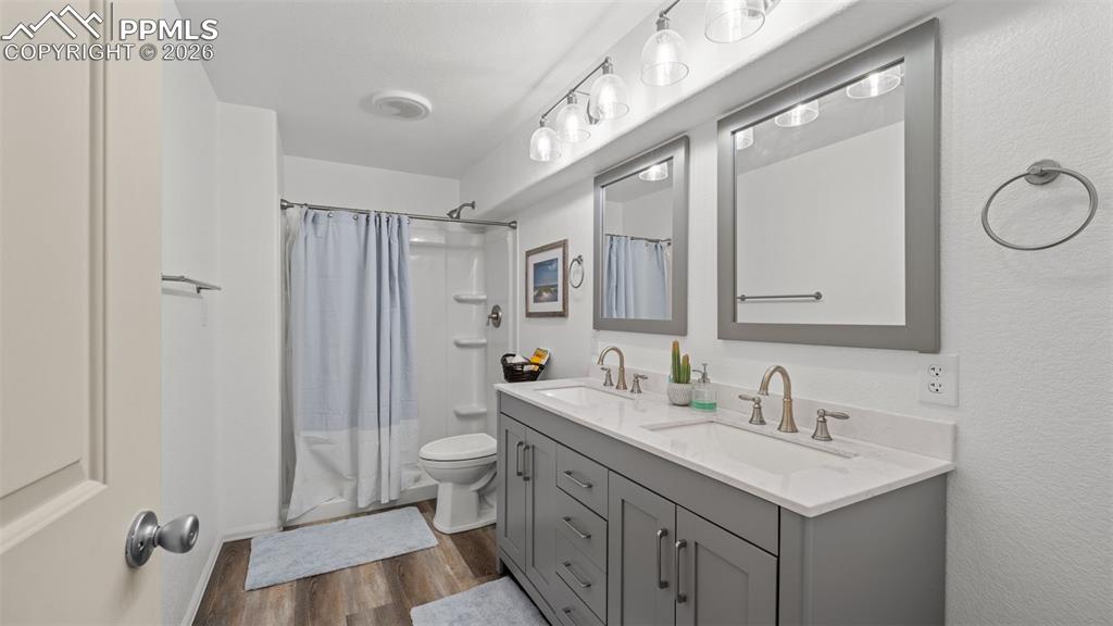 Bathroom with double vanity, dark wood-style flooring, and shower / bath combo with shower curtain