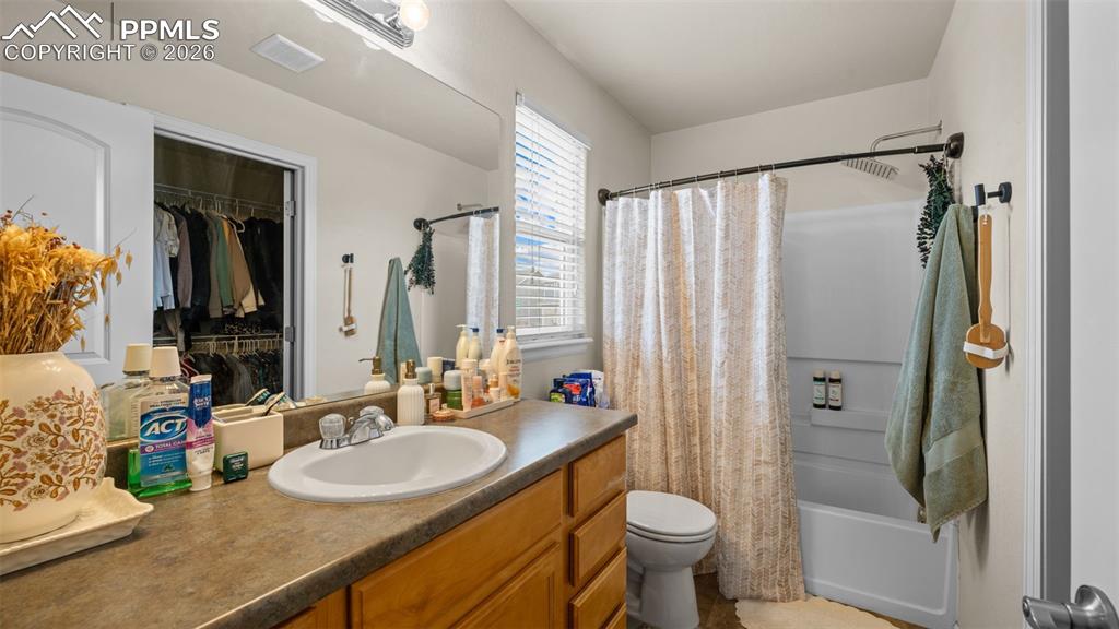 Full bath featuring vanity, shower / tub combo with curtain, and a walk in closet