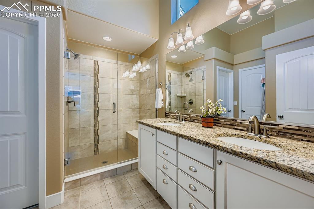 Granite counter w/under mounted sinks, seamless glass shower and tiled flooring 