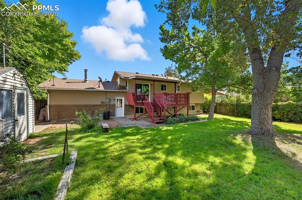 Back of property with stairs, brick siding, a wooden deck, and a storage shed