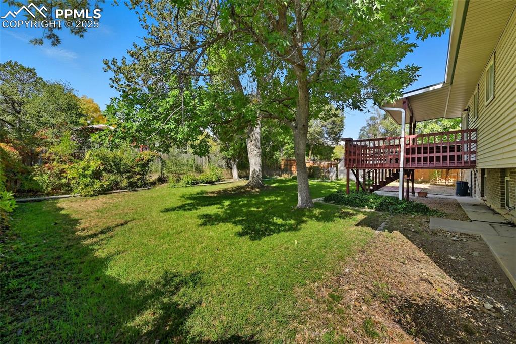 View of grassy yard featuring a deck and stairs