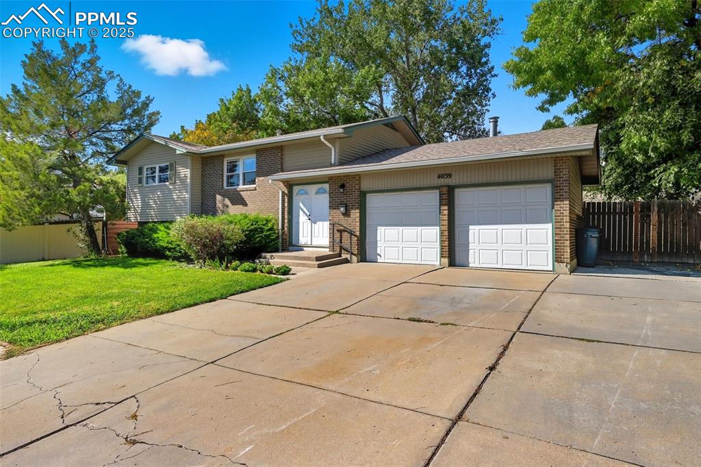 Tri-level home with concrete driveway, an attached garage, brick siding, and a shingled roof