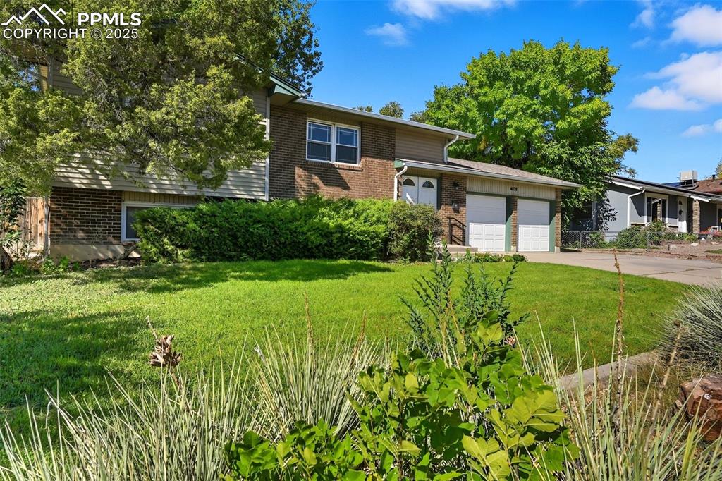 Tri-level home with brick siding, a front lawn, driveway, and an attached garage