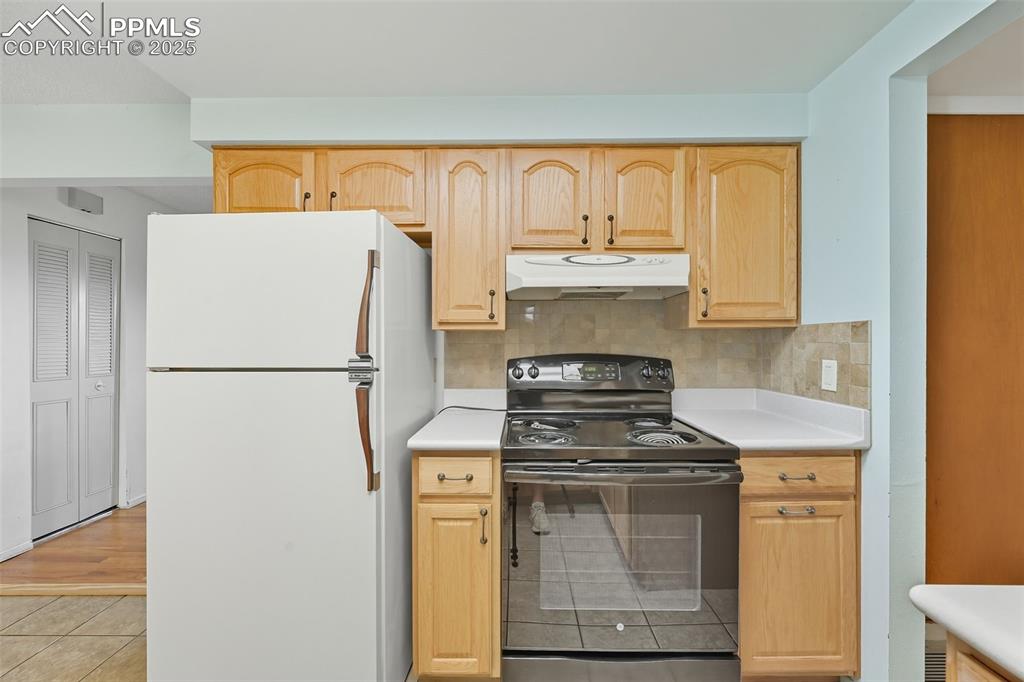 Kitchen featuring black range with electric cooktop, freestanding refrigerator, light countertops, and light brown cabinetry