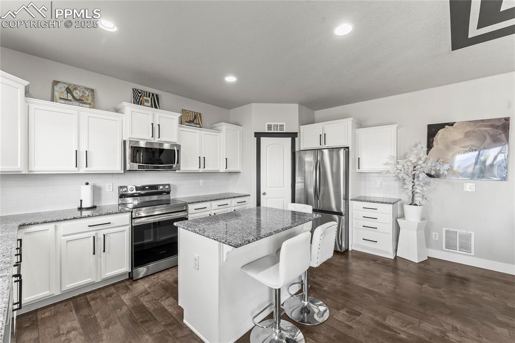 Kitchen with decorative backsplash, stainless steel appliances, white cabinetry, a kitchen bar, and a kitchen island