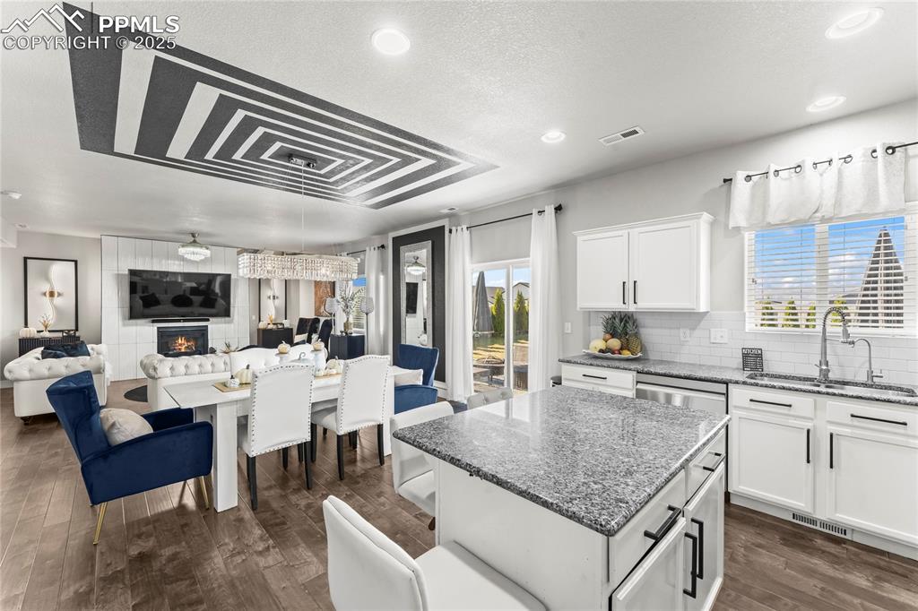 Kitchen with dark stone countertops, white cabinets, open floor plan, a fireplace, and recessed lighting