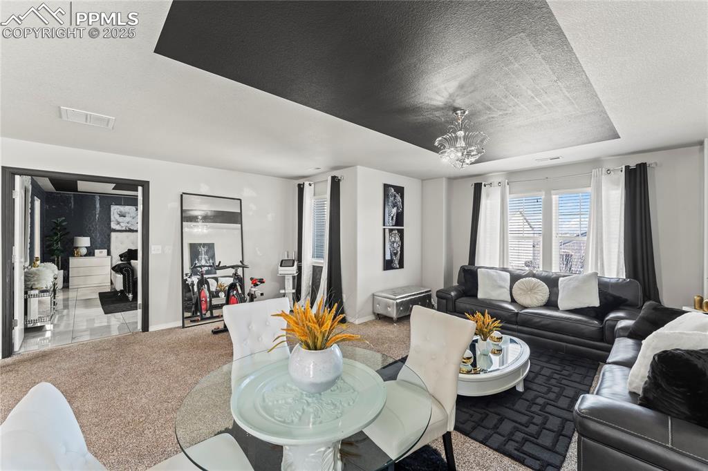 Dining space featuring carpet, a textured ceiling, a raised ceiling, and a chandelier