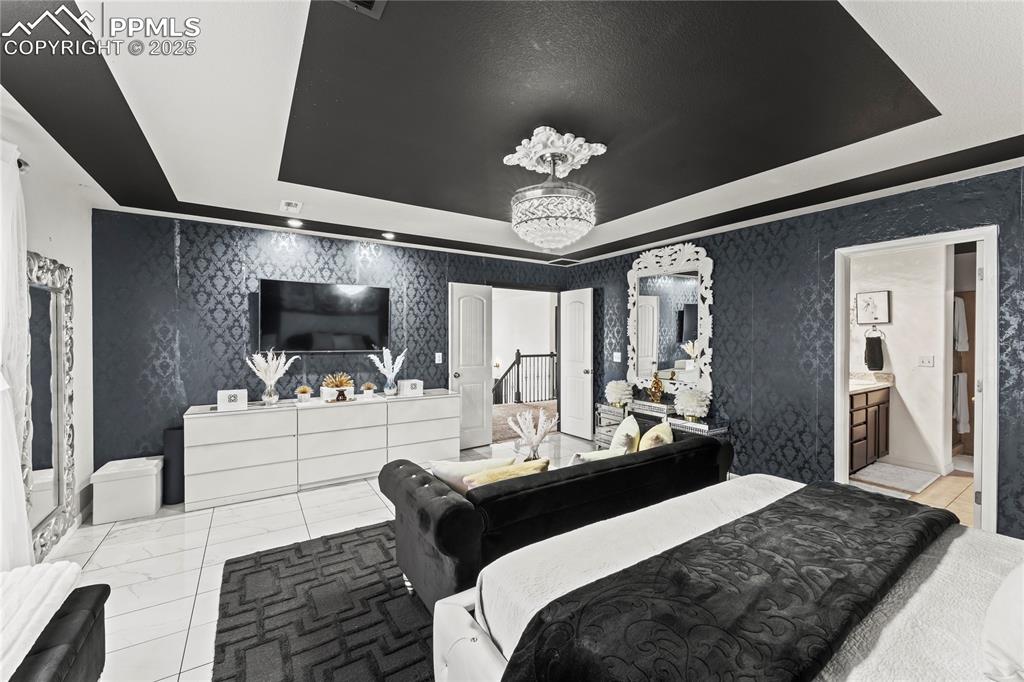 Bedroom with a tray ceiling, wallpapered walls, and ensuite bathroom