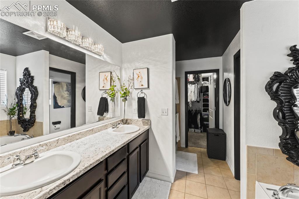 Bathroom with a garden tub, double vanity, a spacious closet, light tile patterned flooring, and a textured ceiling