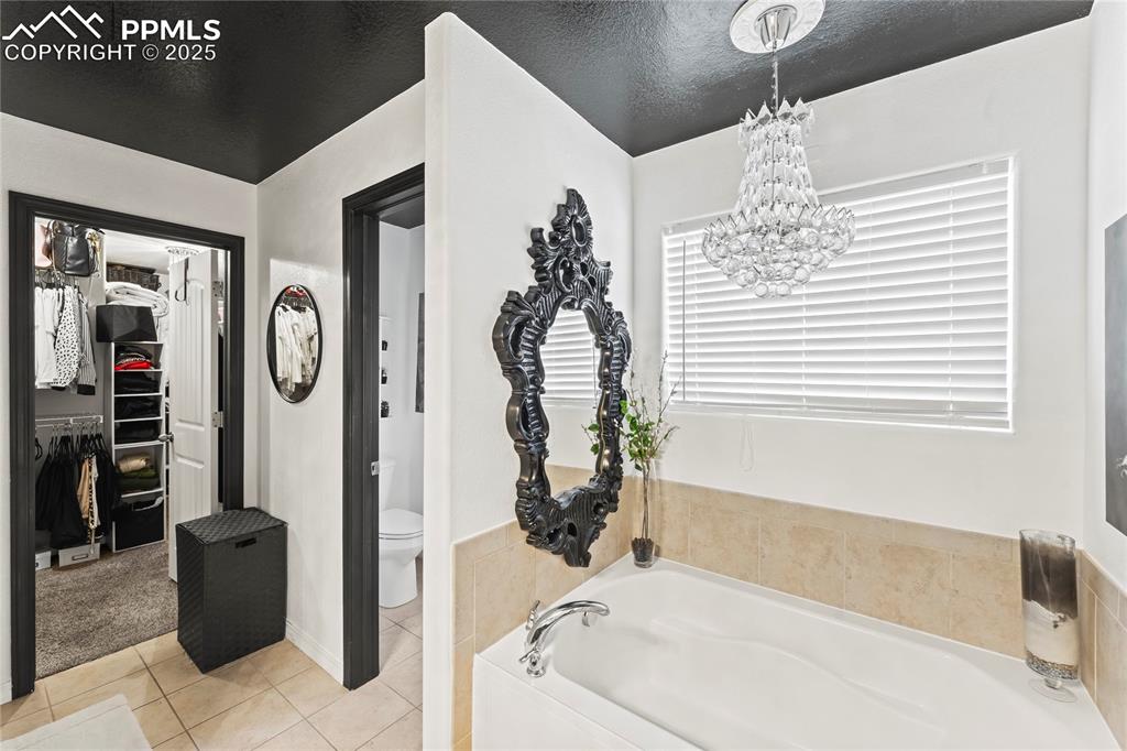 Bathroom with a walk in closet, tile patterned floors, a bath, a textured ceiling, and a chandelier