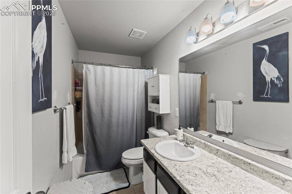 Full bath with vanity, shower / bath combo with shower curtain, and light tile patterned floors