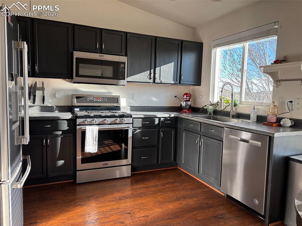 Kitchen featuring stainless steel appliances, dark cabinets, dark wood finished floors, vaulted ceiling, and dark countertops