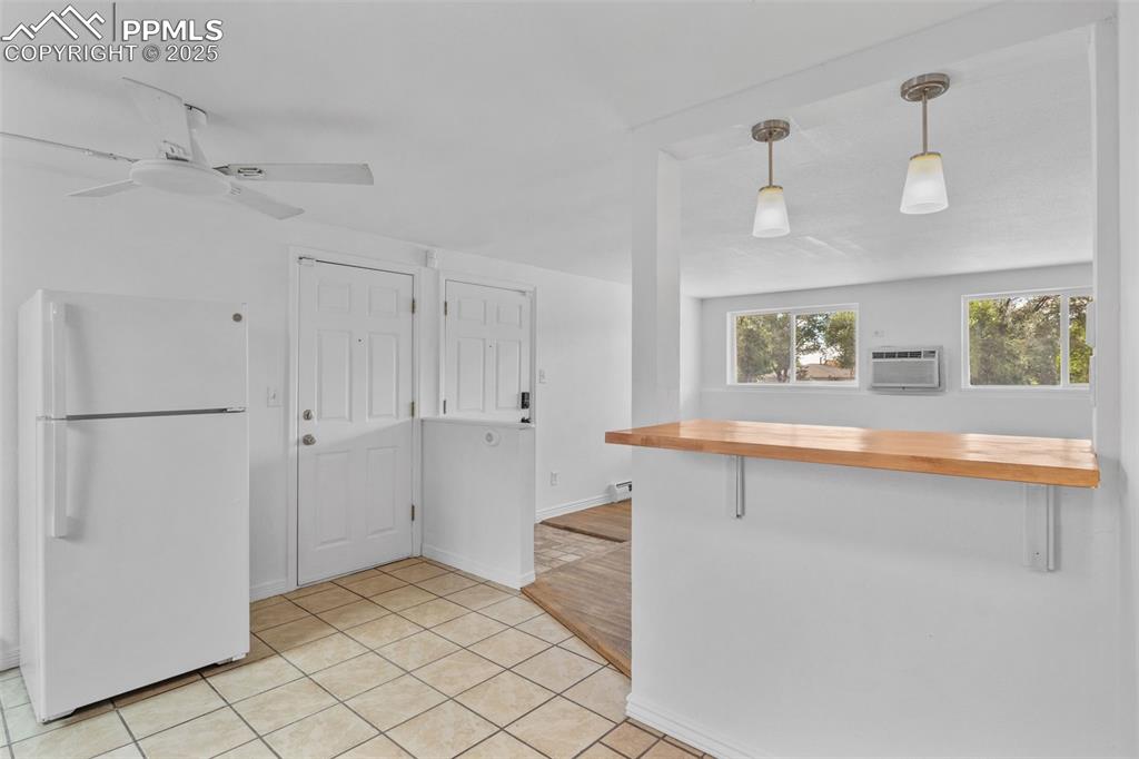 Kitchen with wooden counters, freestanding refrigerator, pendant lighting, light tile patterned flooring, and a peninsula