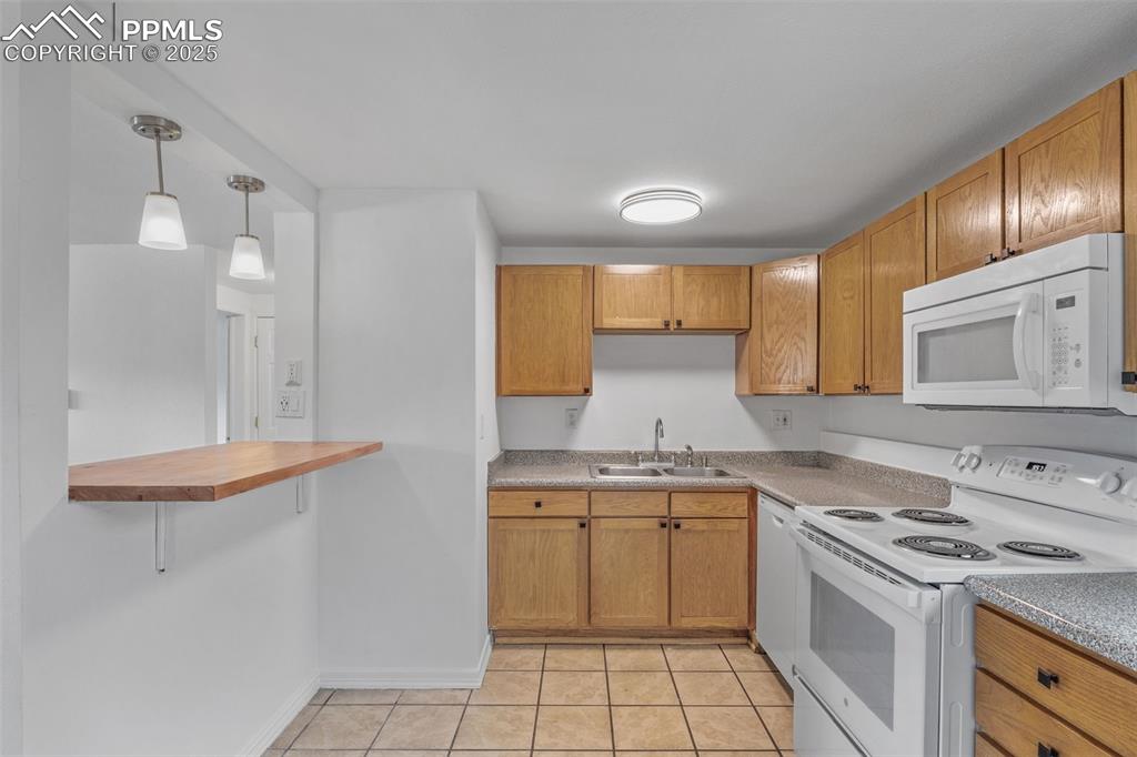 Kitchen with white appliances, pendant lighting, brown cabinetry, a breakfast bar area, and light tile patterned floors