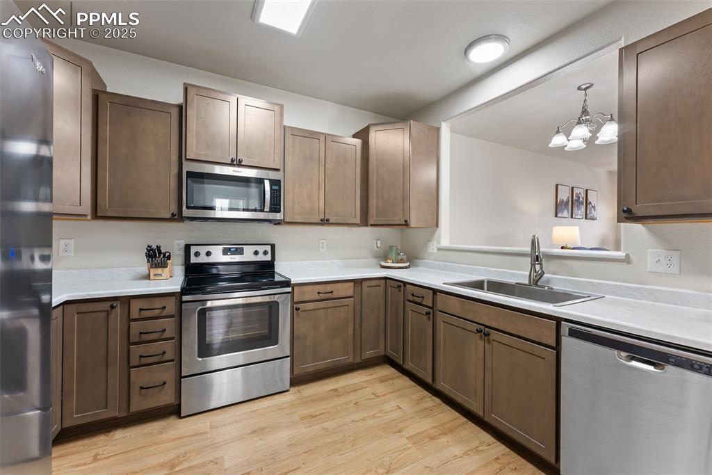 Kitchen with stainless steel appliances, light wood-style floors, light countertops, hanging light fixtures, and a chandelier