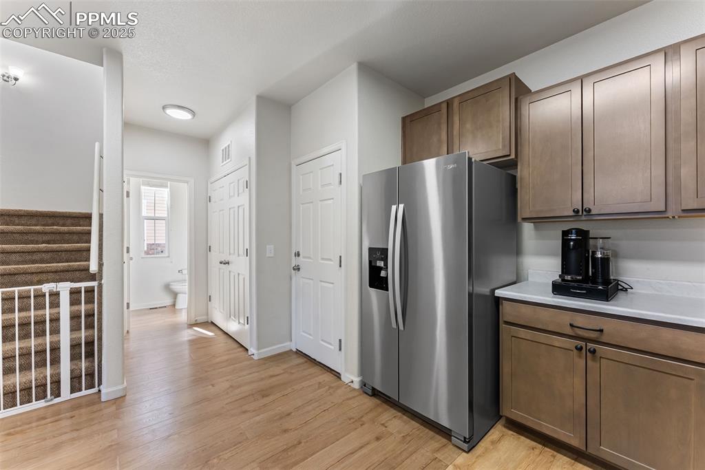 Kitchen with stainless steel fridge with ice dispenser, light countertops, light wood-style flooring, and brown cabinetry